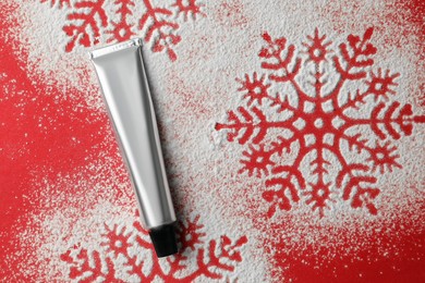 Winter skin care. Hand cream and snowflake silhouettes made with artificial snow on red background, top view