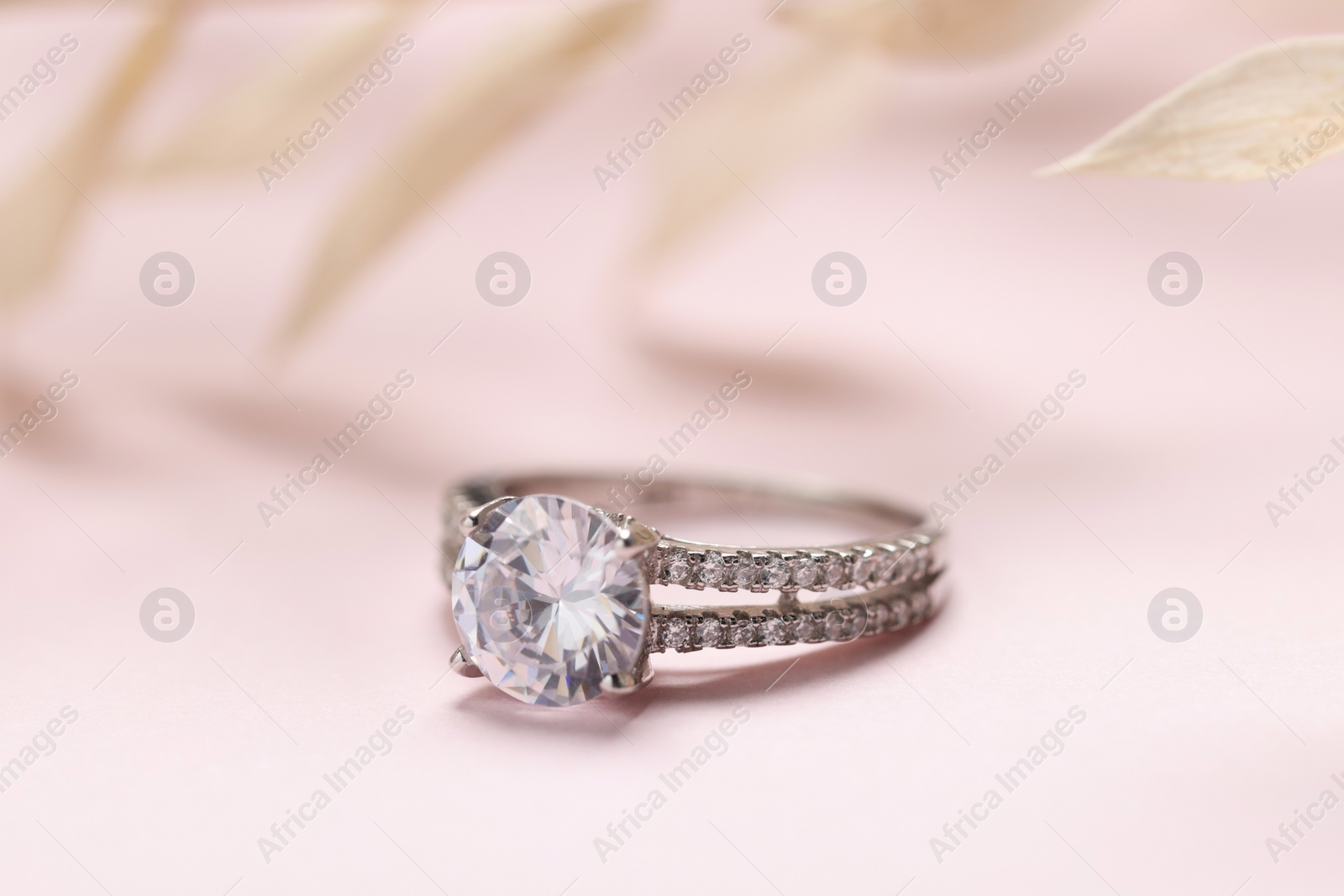 Photo of Beautiful ring with gemstones on pale pink background, closeup. Luxury jewelry