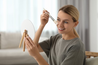 Photo of Young woman applying face mask in frontmirror indoors. Spa treatments