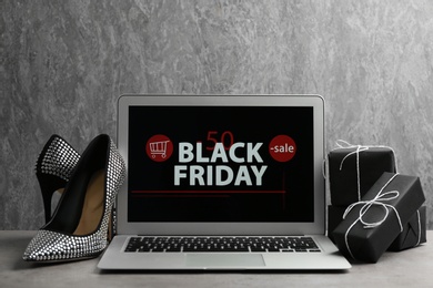 Photo of Laptop with Black Friday announcement, shoes and gifts on table against grey background