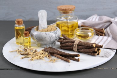 Photo of Dried sticks of licorice roots, powder and essential oil on grey wooden table