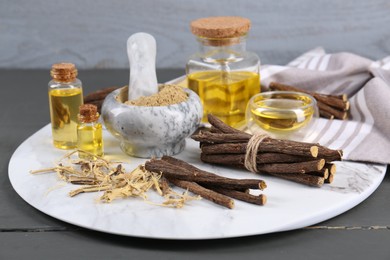 Dried sticks of licorice roots, powder and essential oil on grey wooden table