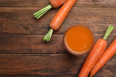 Flat lay composition with carrots and juice on wooden table, space for text