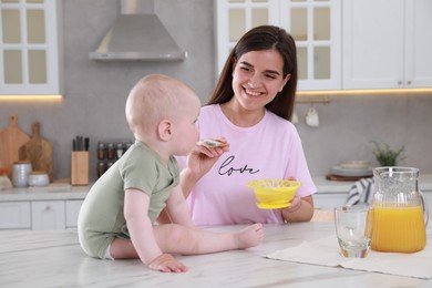 Photo of Happy young woman feeding her cute little baby at table in kitchen