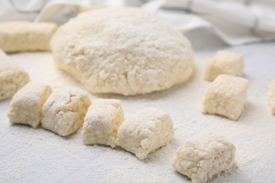 Photo of Making lazy dumplings. Raw dough and flour on white tiled table, closeup