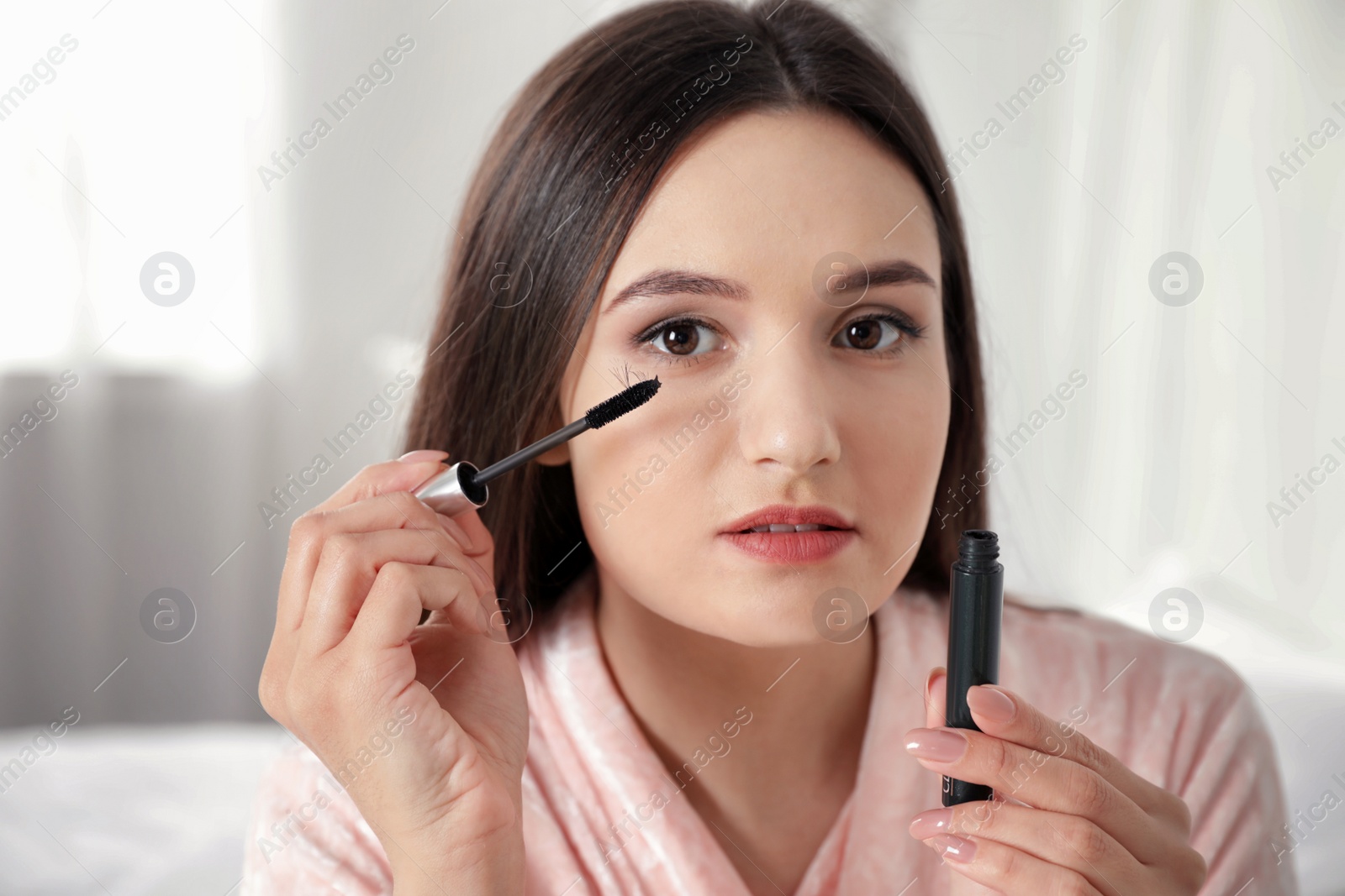 Photo of Beautiful woman holding mascara brush with fallen eyelashes indoors