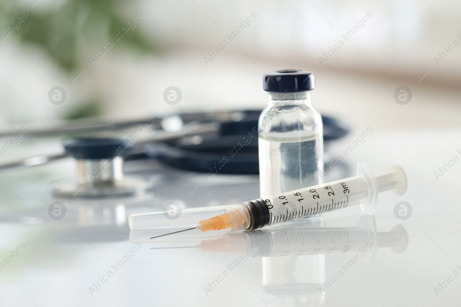 Photo of Glass vial, syringe and stethoscope on white table, closeup