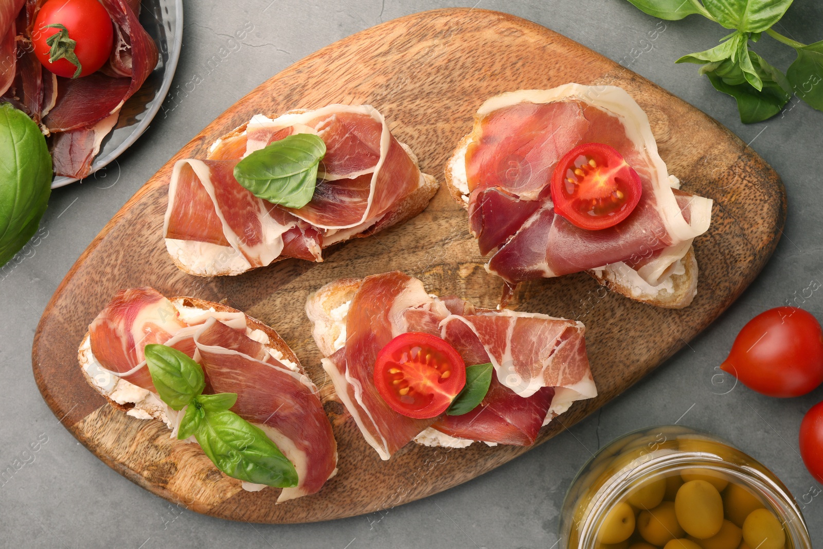 Photo of Tasty sandwiches with cured ham, basil and tomatoes on grey textured table, flat lay