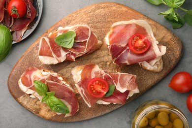 Tasty sandwiches with cured ham, basil and tomatoes on grey textured table, flat lay