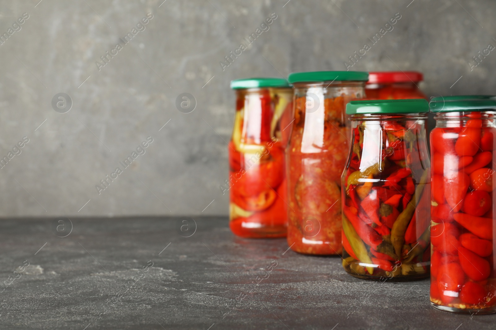 Photo of Jars of tasty pickled vegetables on grey table. Space for text