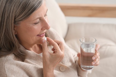 Photo of Senior woman with glass of water taking pill indoors, closeup