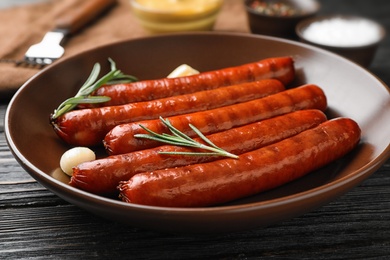 Delicious grilled sausages in bowl on dark wooden table. Barbecue food