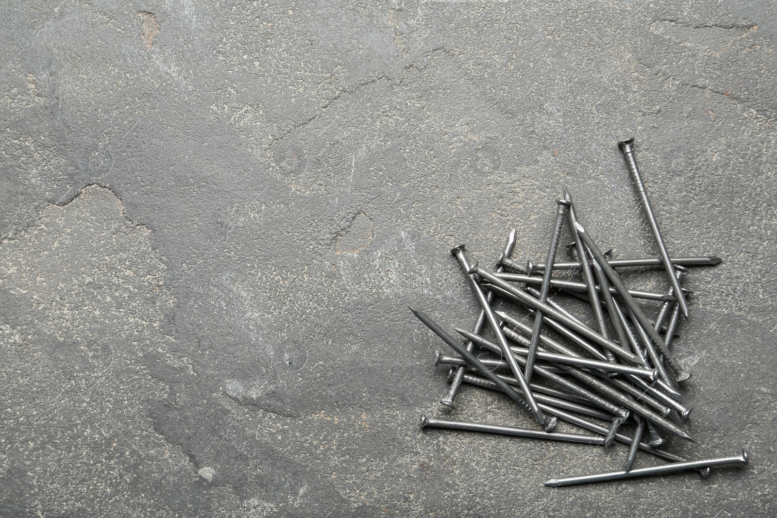 Photo of Pile of metal nails on grey stone background, flat lay. Space for text