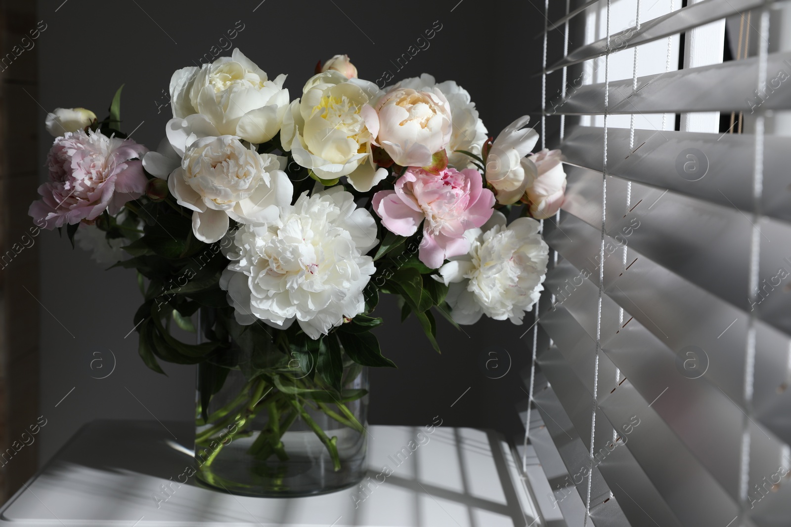 Photo of Beautiful peonies in vase on table near window indoors