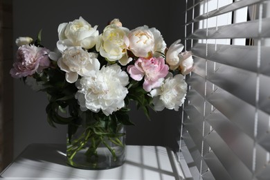 Beautiful peonies in vase on table near window indoors