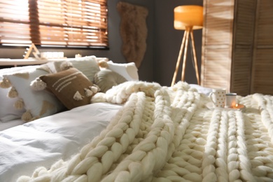 Photo of Bed with cozy knitted blanket and cushions near window in room. Interior design