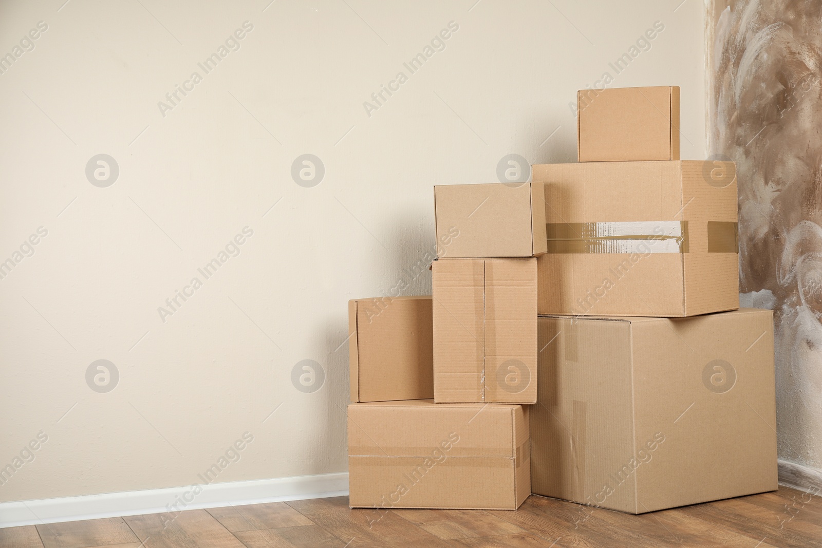 Photo of Pile of cardboard boxes near light wall indoors. Space for text