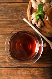 Cup of delicious ginger tea and honey on wooden table, flat lay
