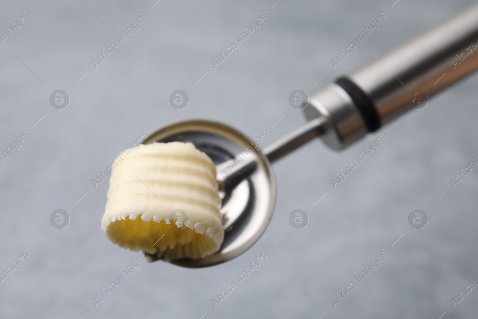 Photo of Tasty butter curl in spoon on light grey table, closeup