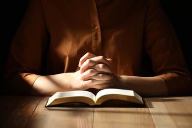 Photo of Religious woman praying over Bible at wooden table indoors, closeup