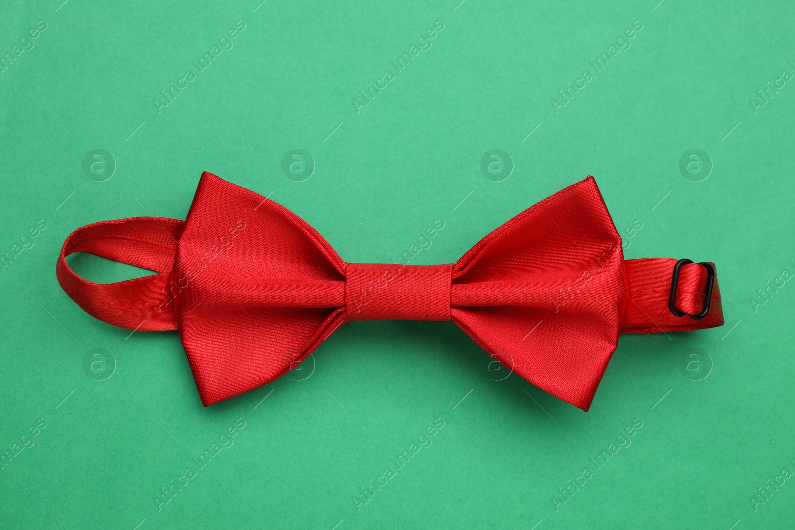 Photo of Stylish red bow tie on green background, top view