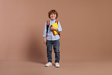 Happy schoolboy with backpack and books on brown background