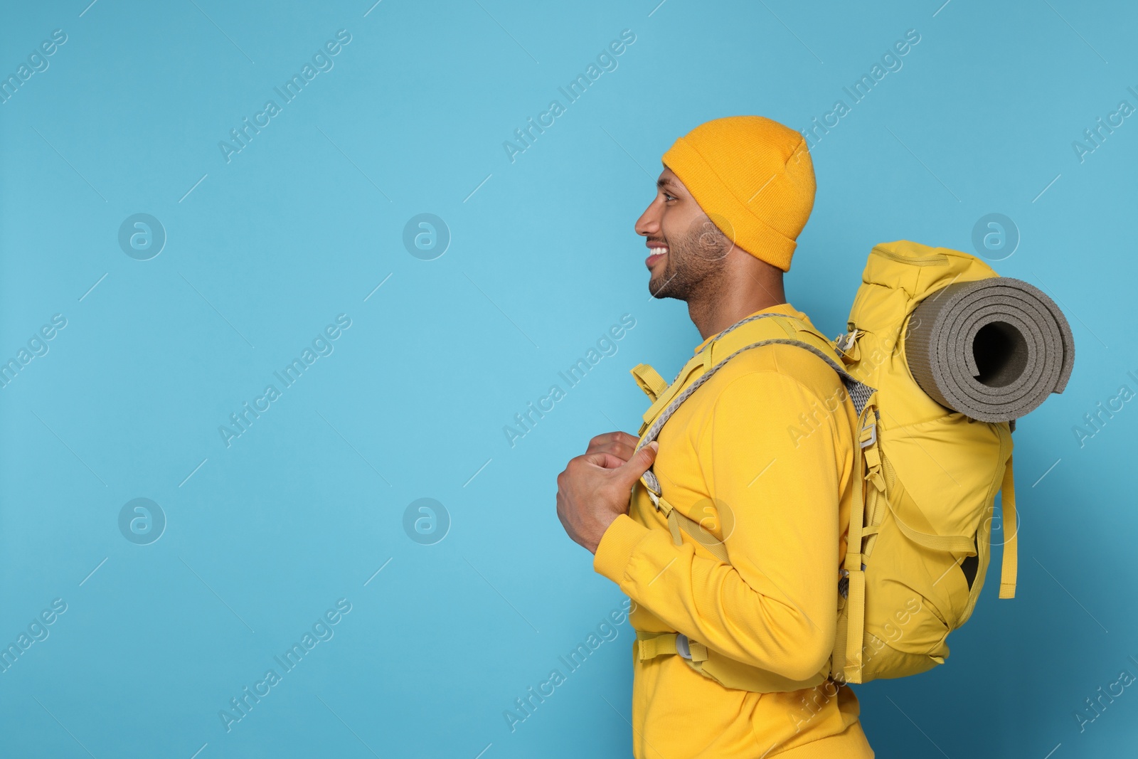 Photo of Happy tourist with backpack on light blue background, space for text