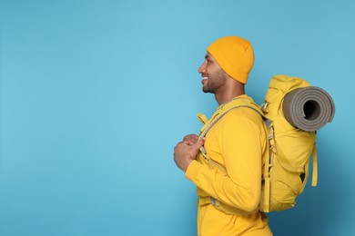 Photo of Happy tourist with backpack on light blue background, space for text