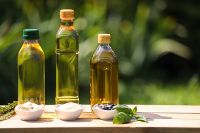 Different cooking oils and ingredients on wooden table against blurred green background. Space for text