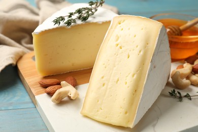 Photo of Tasty Camembert cheese with thyme, honey and nuts on light blue wooden table, closeup