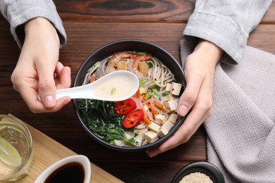 Photo of Woman eating delicious ramen with spoon at wooden table, top view. Noodle soup