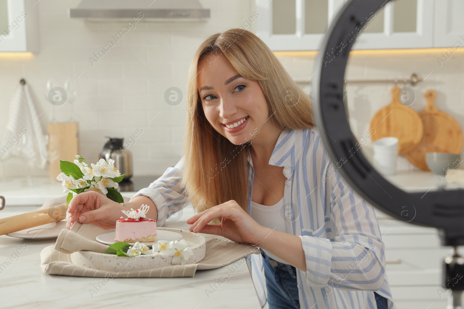 Photo of Blogger with tasty cake and ring lamp recording video in kitchen at home