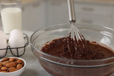 Photo of Metal whisk, chocolate cream in bowl and different products on gray table indoors, closeup