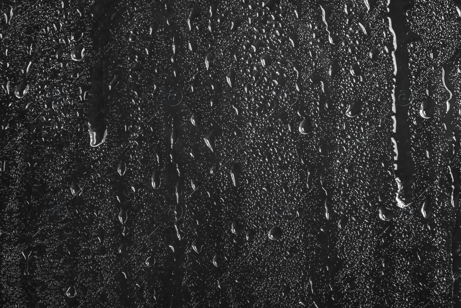 Photo of Glass with rain drops against dark background