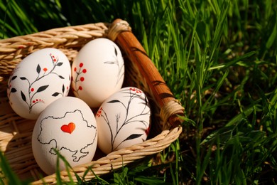 Photo of Wicker basket with decorated Easter eggs in green grass outdoors, closeup. Space for text