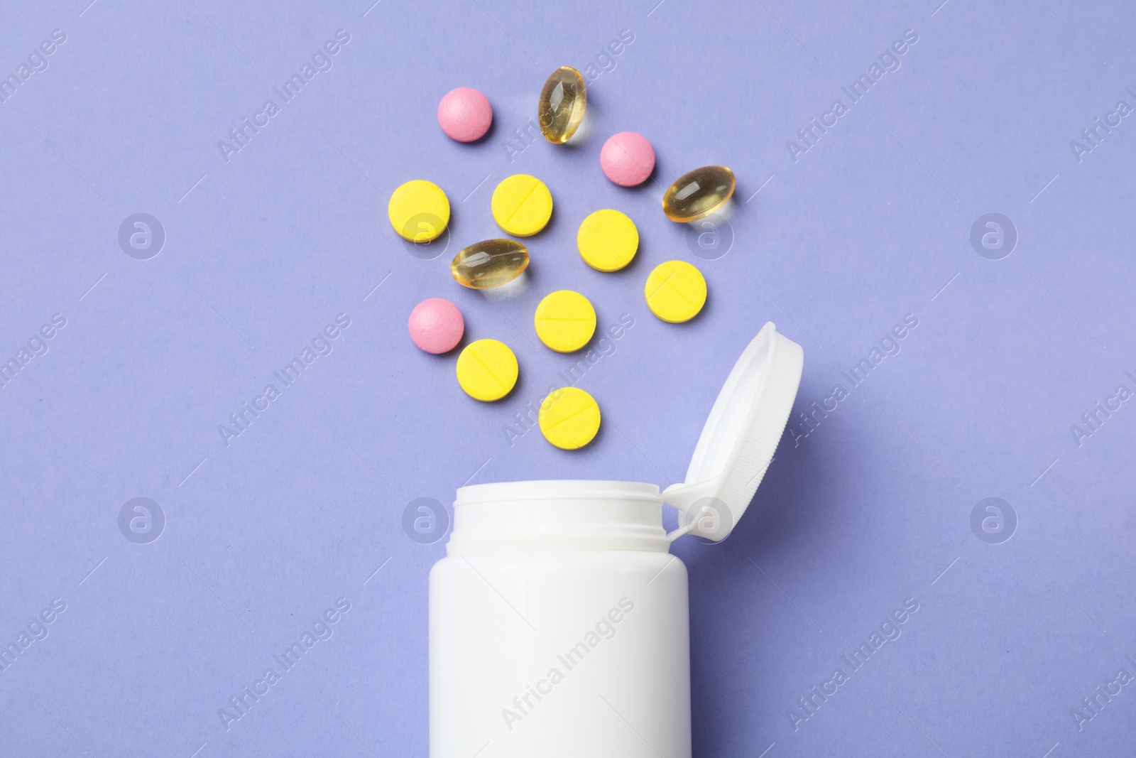 Photo of White bottle and different vitamin pills on violet background, top view