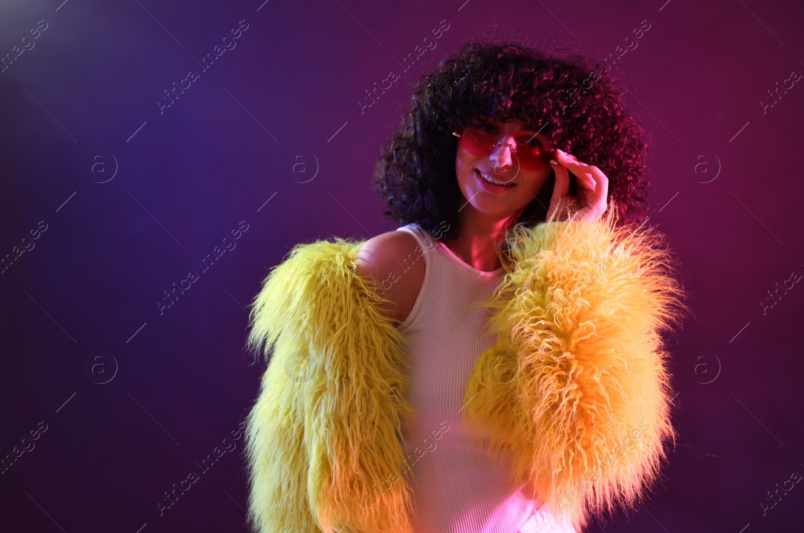 Photo of Beautiful young woman in yellow fur coat and sunglasses on color background in neon lights