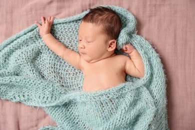 Cute newborn baby in turquoise knitted blanket lying on bed, top view