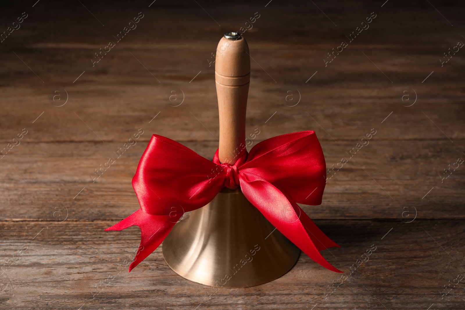 Photo of Golden bell with red bow on wooden table. School days