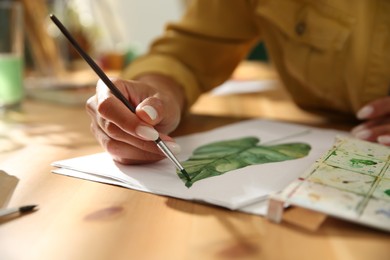 Photo of Young woman drawing leaf at table, closeup