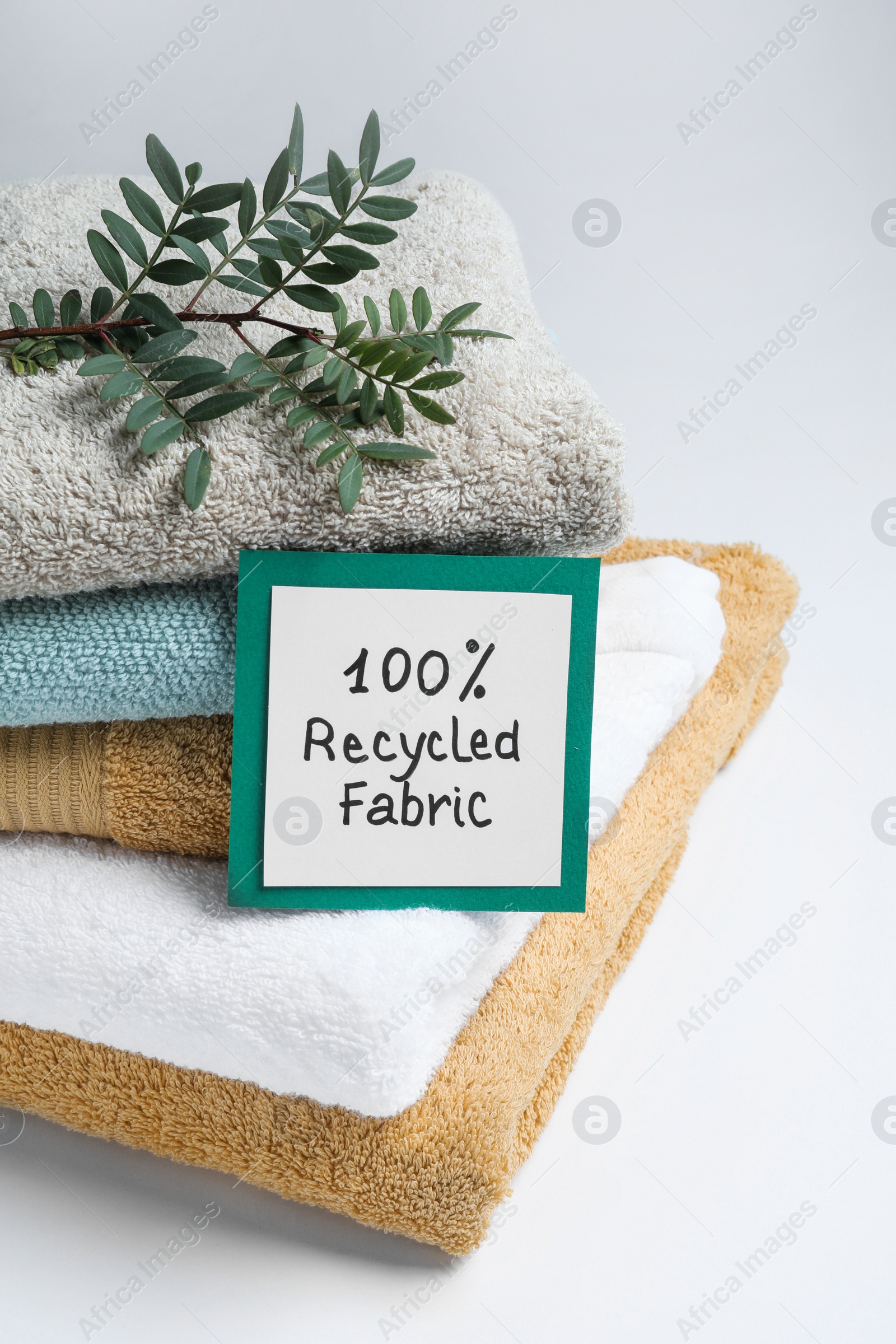 Photo of Recycling concept. Stacked towels and card with plant on white background, closeup