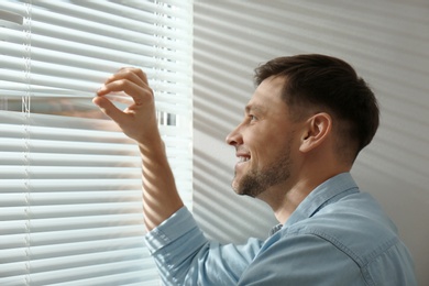 Handsome man opening window blinds at home