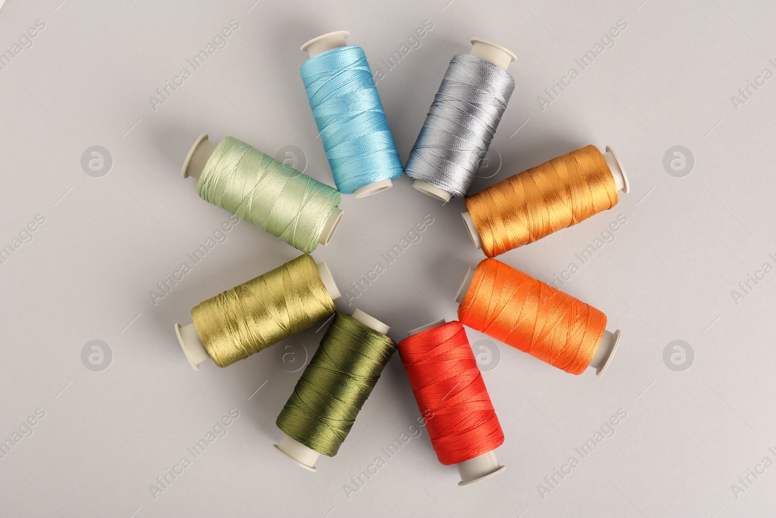 Photo of Different colorful sewing threads on light grey background, flat lay