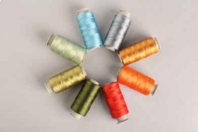 Different colorful sewing threads on light grey background, flat lay