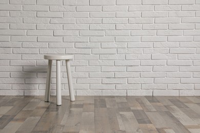 Photo of Stylish stool near white brick wall indoors. Space for text