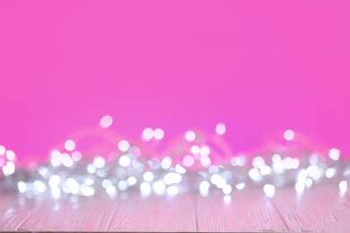 Photo of White Christmas lights on pink wooden table, blurred view