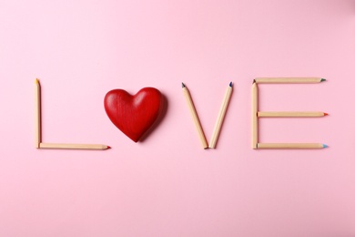 Photo of Word LOVE made of pencils and decorative heart on pink background, flat lay
