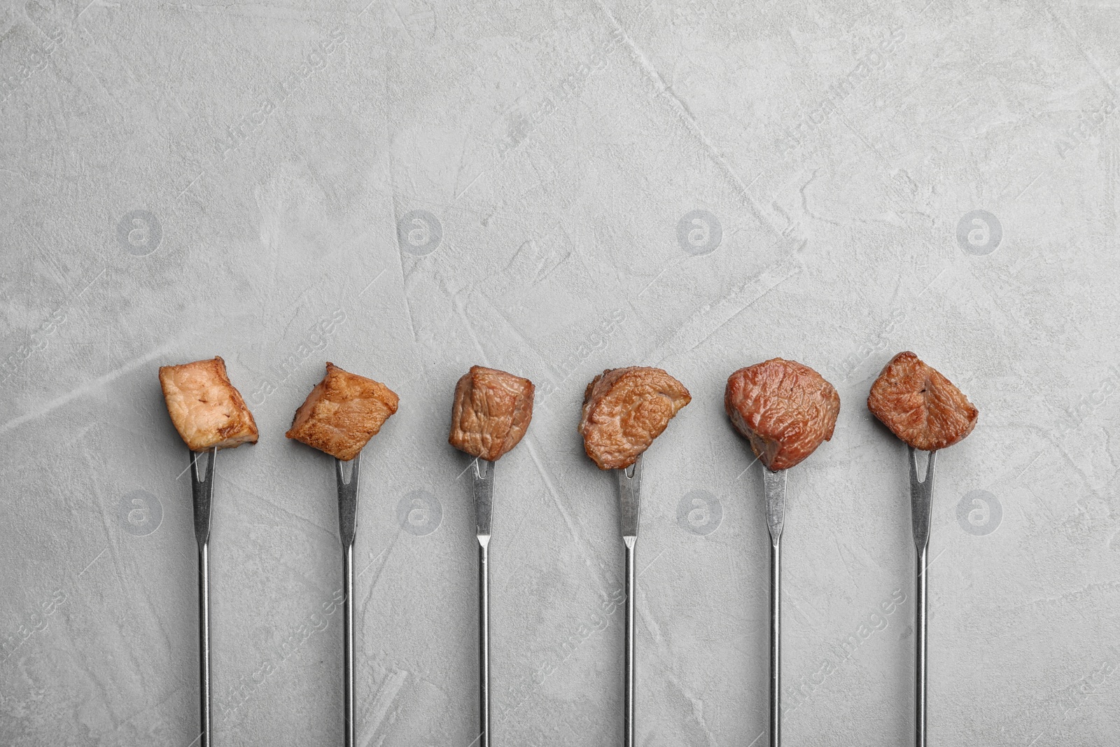 Photo of Forks with fried meat fondue pieces on grey background, top view. Space for text