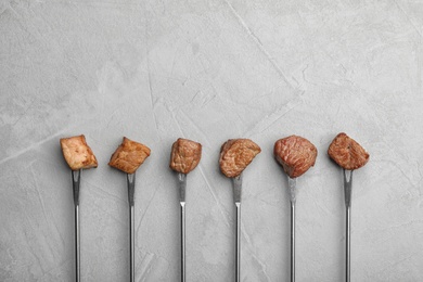 Photo of Forks with fried meat fondue pieces on grey background, top view. Space for text