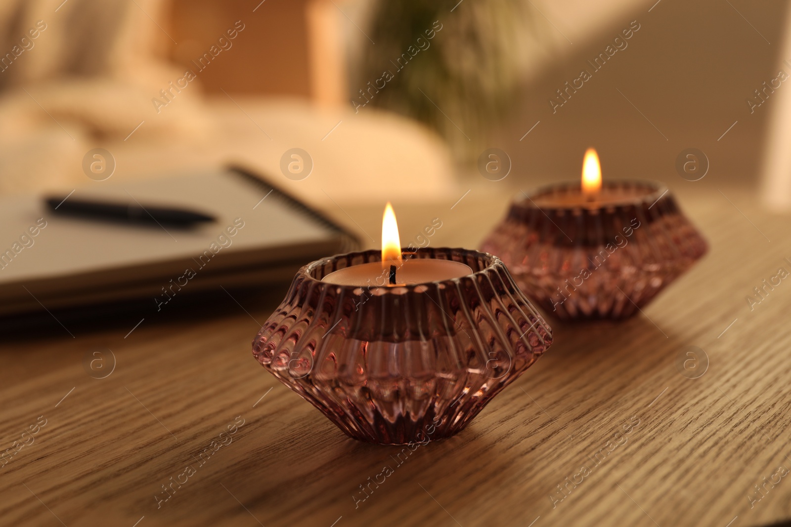 Photo of Burning candles in beautiful glass holders on wooden table indoors, closeup